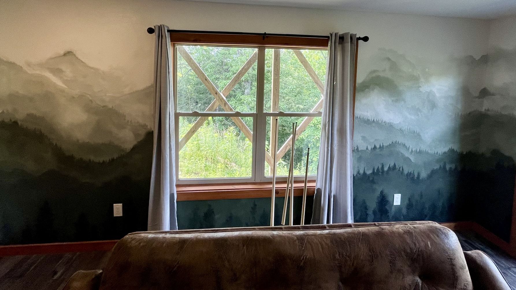 Deep green mountain and forest mural filling a living room wall around a window