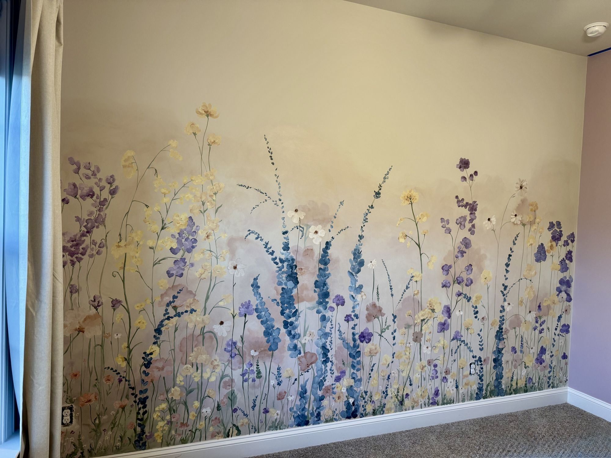 Hand-painted wildflower meadow nursery mural in Mint Hill, NC, blues, purples and yellows running the length of the wall